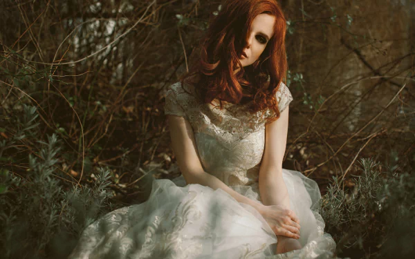 Redheaded model in a lace wedding dress seated in a shadowy woodland, a bride portrait rendered as a 4K Ultra HD desktop wallpaper.