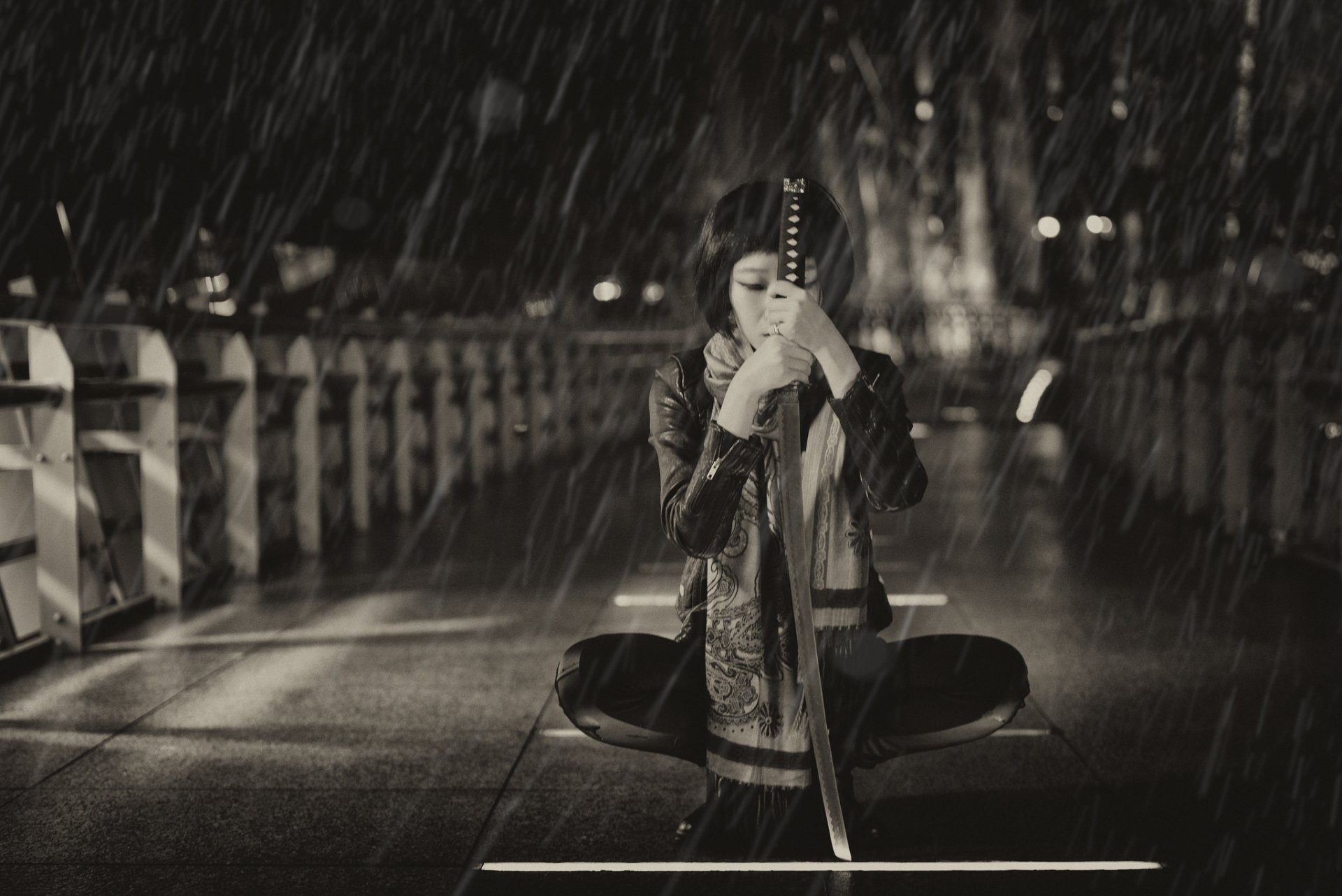 A martial artist kneeling on a rain-soaked bridge, gripping a katana, captured in a dramatic black-and-white HD desktop wallpaper.