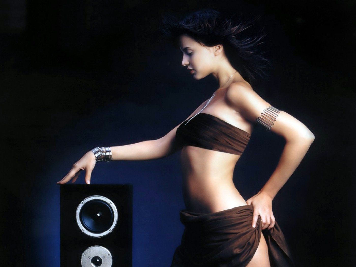 A striking HD desktop wallpaper featuring a woman in a stylish pose beside a sleek music speaker, highlighting the connection between beauty and sound.