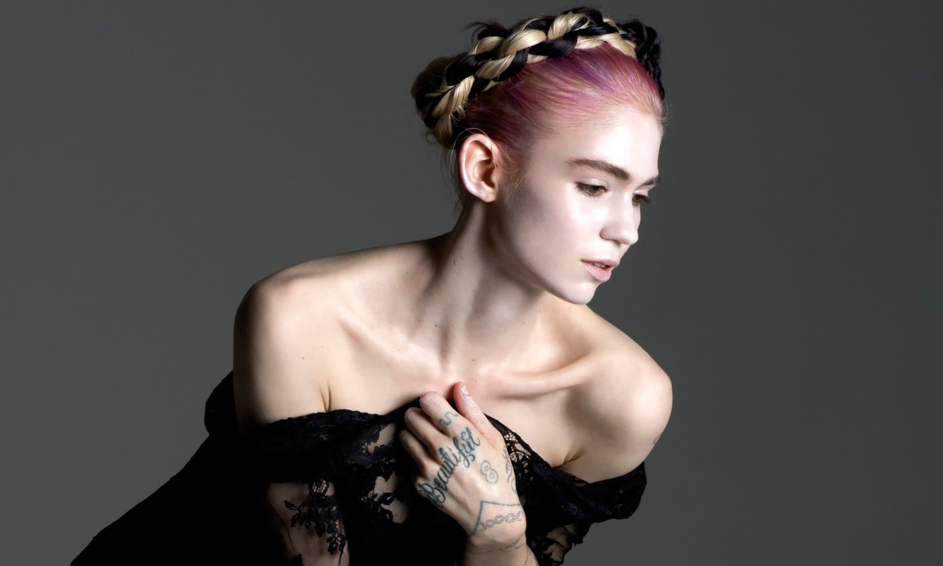 HD desktop wallpaper featuring Canadian singer Grimes with pink hair, braided crown, and visible hand tattoos against a dark gray background.