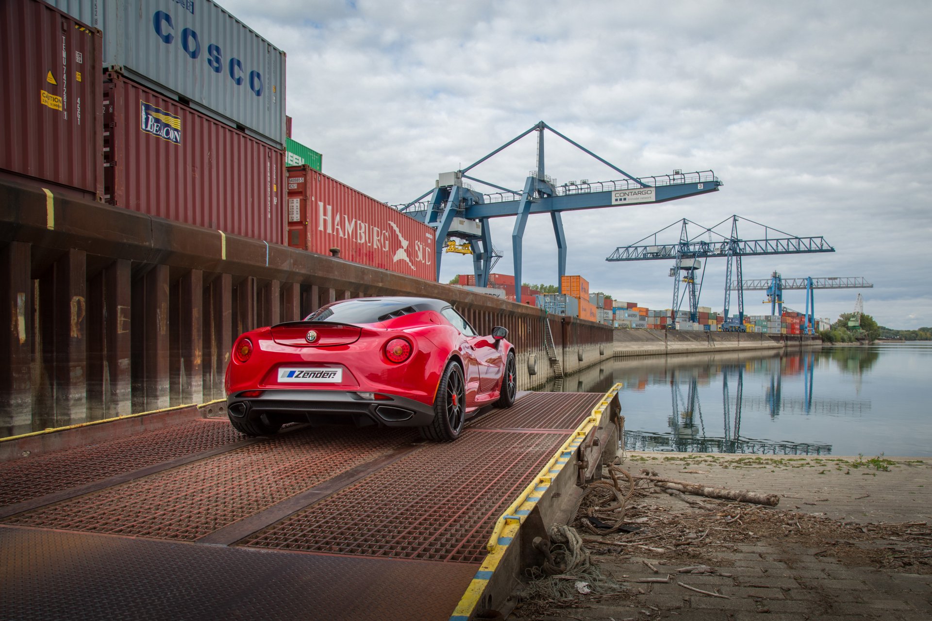 Red Alfa Romeo 4C parked on a dockside ramp by shipping containers and cranes, captured in a 4K Ultra HD vehicle wallpaper background.