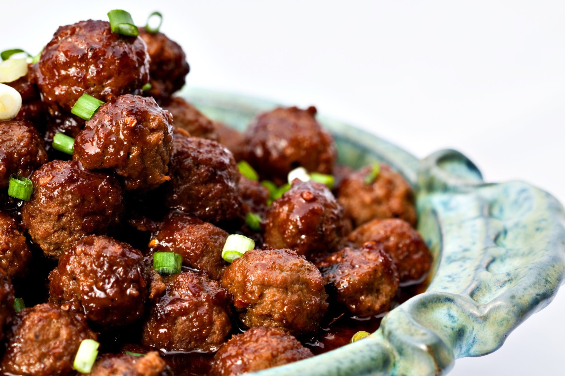 Close-up of glazed meatballs garnished with chopped green onions, presented in a decorative dish, captured in stunning 4K Ultra HD for a vibrant food wallpaper.