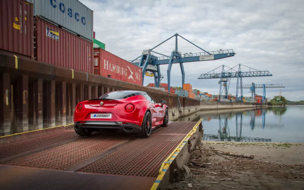 Red Alfa Romeo 4C parked on a dockside ramp by shipping containers and cranes, captured in a 4K Ultra HD vehicle wallpaper background.
