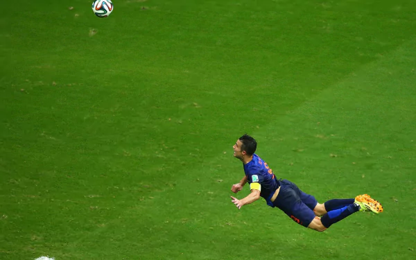 Diving soccer player midair heading a ball on a green pitch, sports action with captain's armband visible — 2K Quad HD PC desktop wallpaper and background.