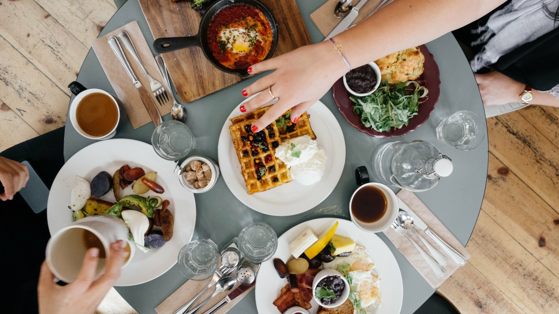 4K Ultra HD PC desktop wallpaper: overhead view of a breakfast table with a waffle, assorted breakfast plates, coffee cups and hands reaching across the meal.