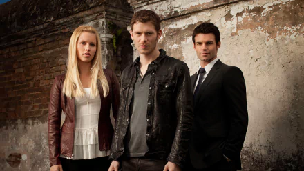Three main characters from the TV show *The Originals* stand against a weathered wall. The image serves as a high-definition desktop wallpaper featuring a dramatic, moody backdrop.