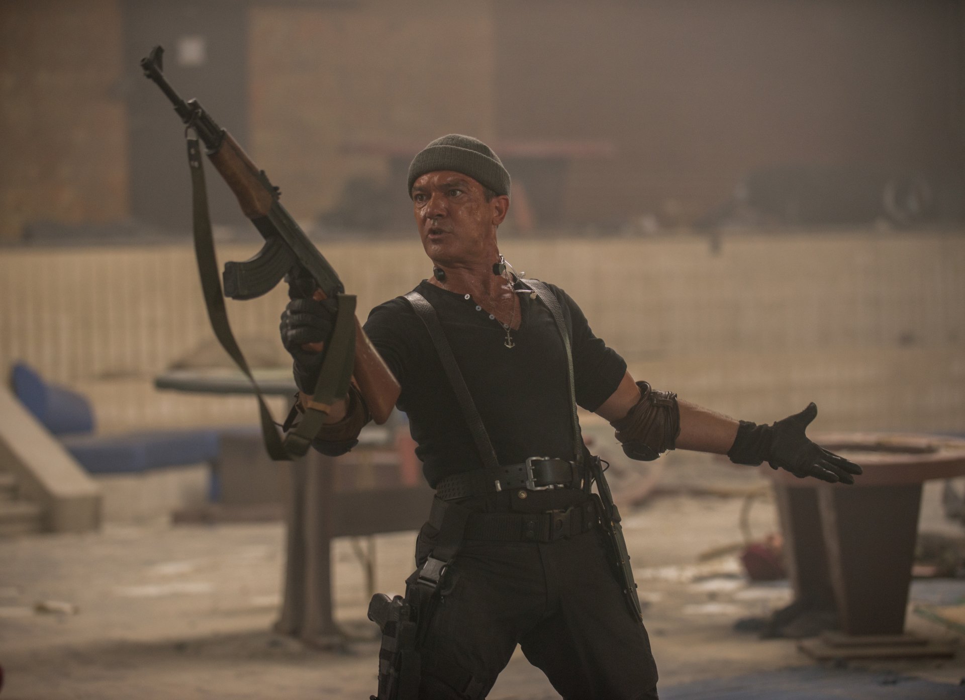 5K Ultra HD wallpaper: armed mercenary in black tactical gear lifts a rifle amid urban rubble, cinematic action vibe from The Expendables 3.