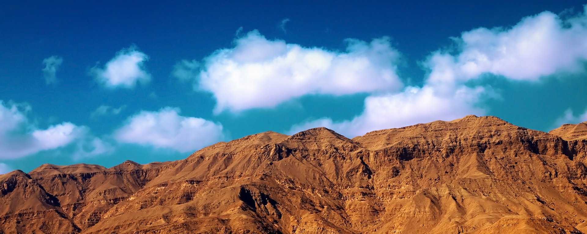 HD PC desktop wallpaper featuring a rugged mountain range under a vibrant blue sky with scattered clouds, capturing the essence of nature's beauty.
