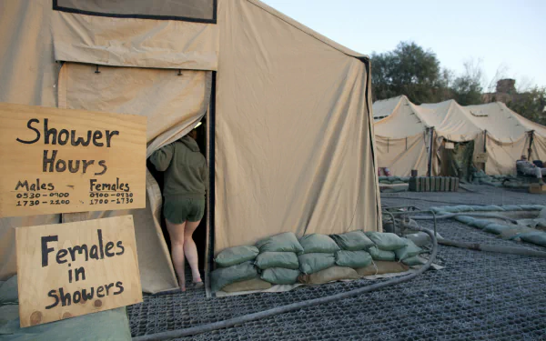 A soldier enters a shower tent, with signs indicating designated shower hours for males and females, set against a backdrop of military tents and surroundings. 4K Ultra HD wallpaper.