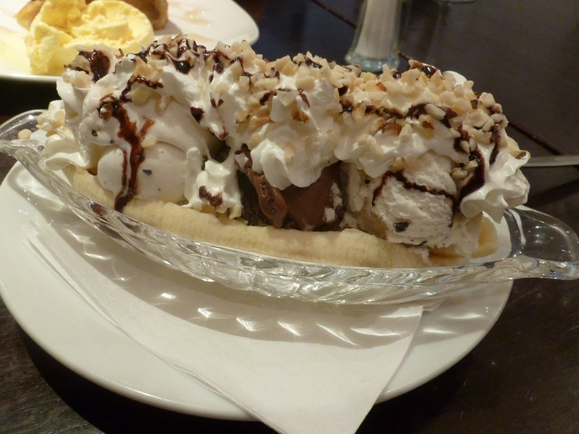 Banana split with scoops of ice cream, whipped cream, nuts and chocolate drizzle on a glass dish — food photo rendered as 4K Ultra HD PC desktop wallpaper and background.