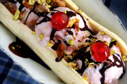 Close-up of a banana split topped with pink ice cream, chocolate syrup, chopped nuts, and bright red cherries, captured in 4K Ultra HD quality for desktop background.