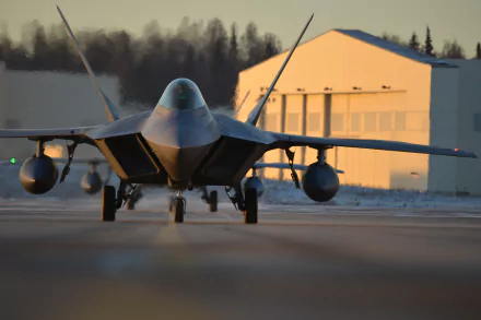 A striking view of a Lockheed Martin F-22 Raptor aircraft on a runway, showcasing its sleek design against a backdrop of military hangars during sunset. 4K Ultra HD wallpaper.