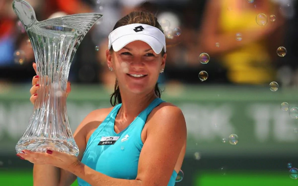 Polish tennis player smiling, holding a crystal trophy amid floating bubbles — HD sports desktop wallpaper and background.