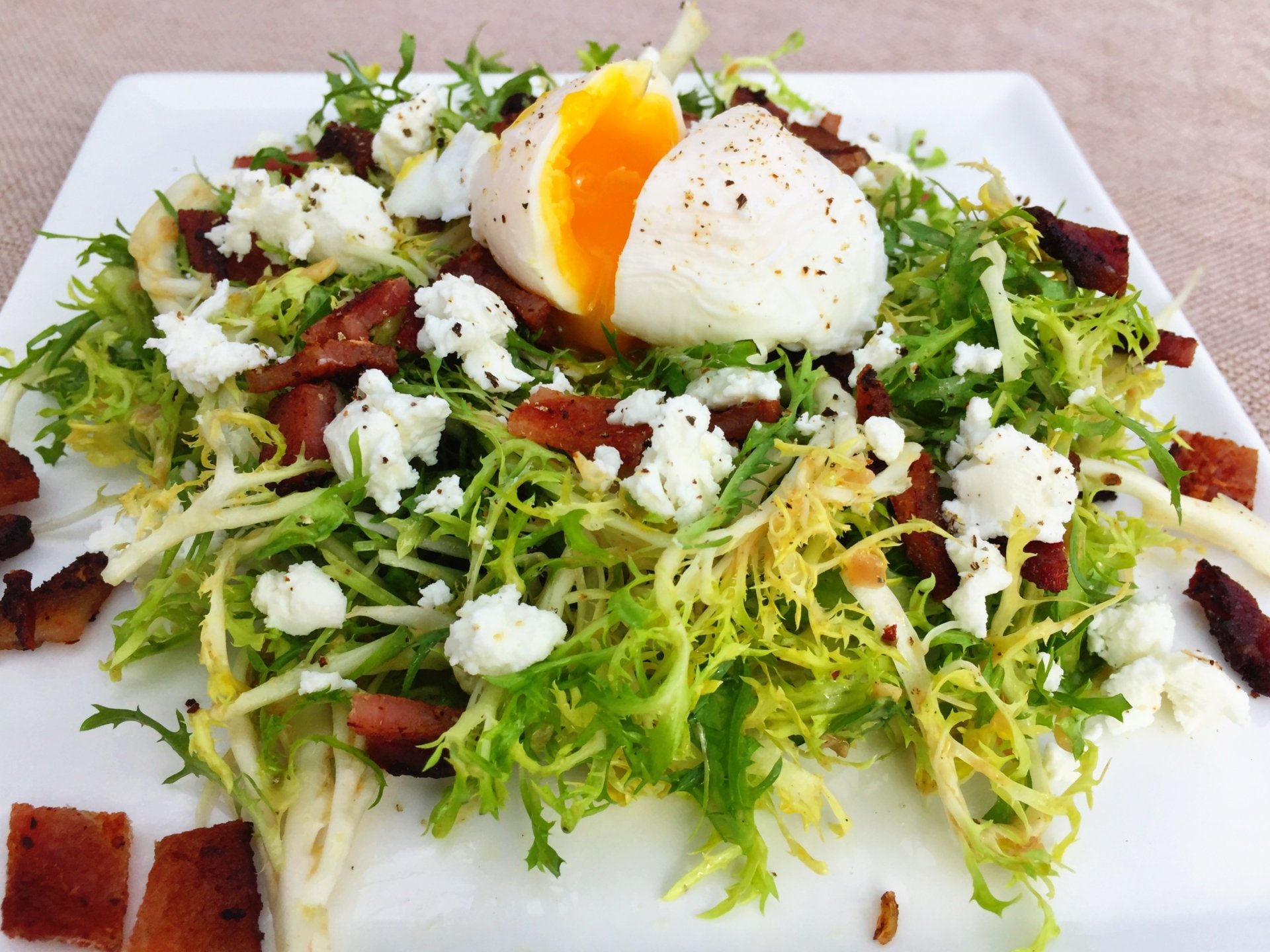 A vibrant Salade Lyonnaise featuring frisée greens, crispy bacon, crumbled cheese, and a soft-boiled egg, presented as an HD PC desktop wallpaper background.