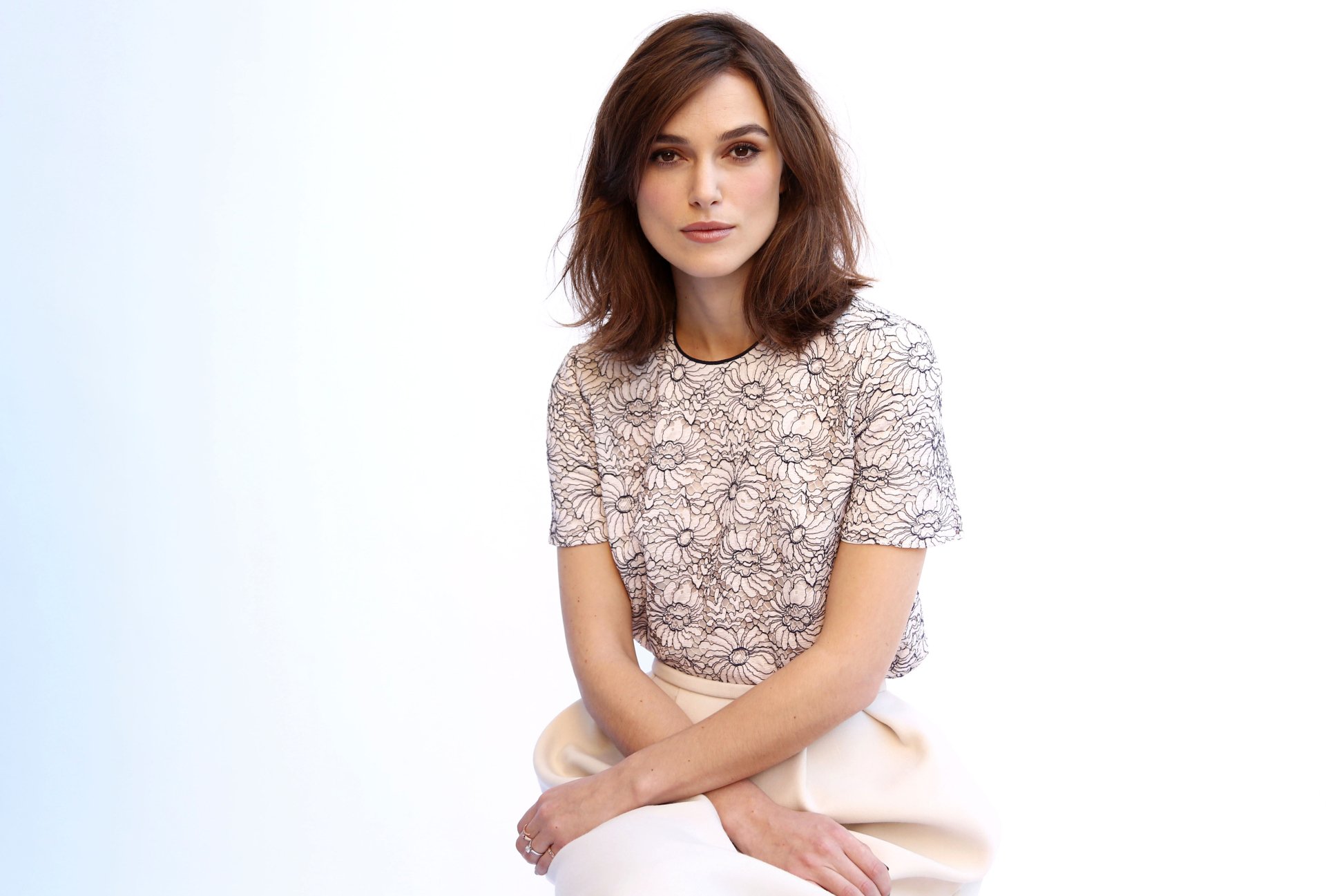 4K Ultra HD PC desktop wallpaper featuring celebrity Keira Knightley sitting against a white background, wearing a patterned top and light-colored pants.