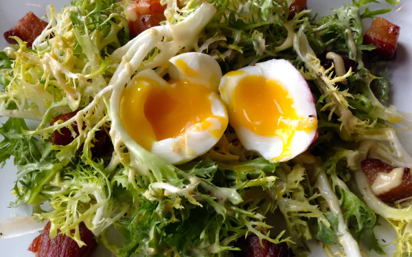 Close-up of a Salade Lyonnaise with a soft-boiled egg, frisée greens, and bacon, captured in HD for a vibrant lunch meal desktop wallpaper.