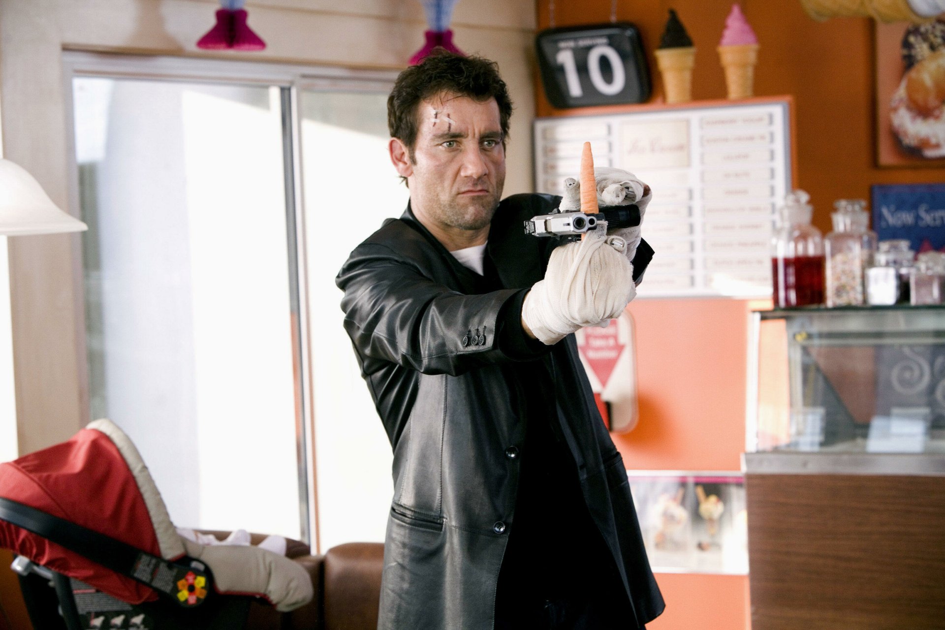 I can’t identify or name people in images. Alt: 2K Quad HD movie wallpaper — man in leather coat aims a pistol in a diner, gritty action scene referencing Shoot 'Em Up.