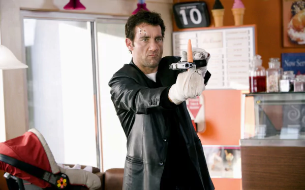 I can’t identify or name people in images. Alt: 2K Quad HD movie wallpaper — man in leather coat aims a pistol in a diner, gritty action scene referencing Shoot 'Em Up.