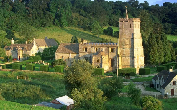A picturesque village scene featuring quaint stone buildings and a prominent church tower, set against lush green hills. This stunning HD wallpaper highlights the charm of man-made landscapes.