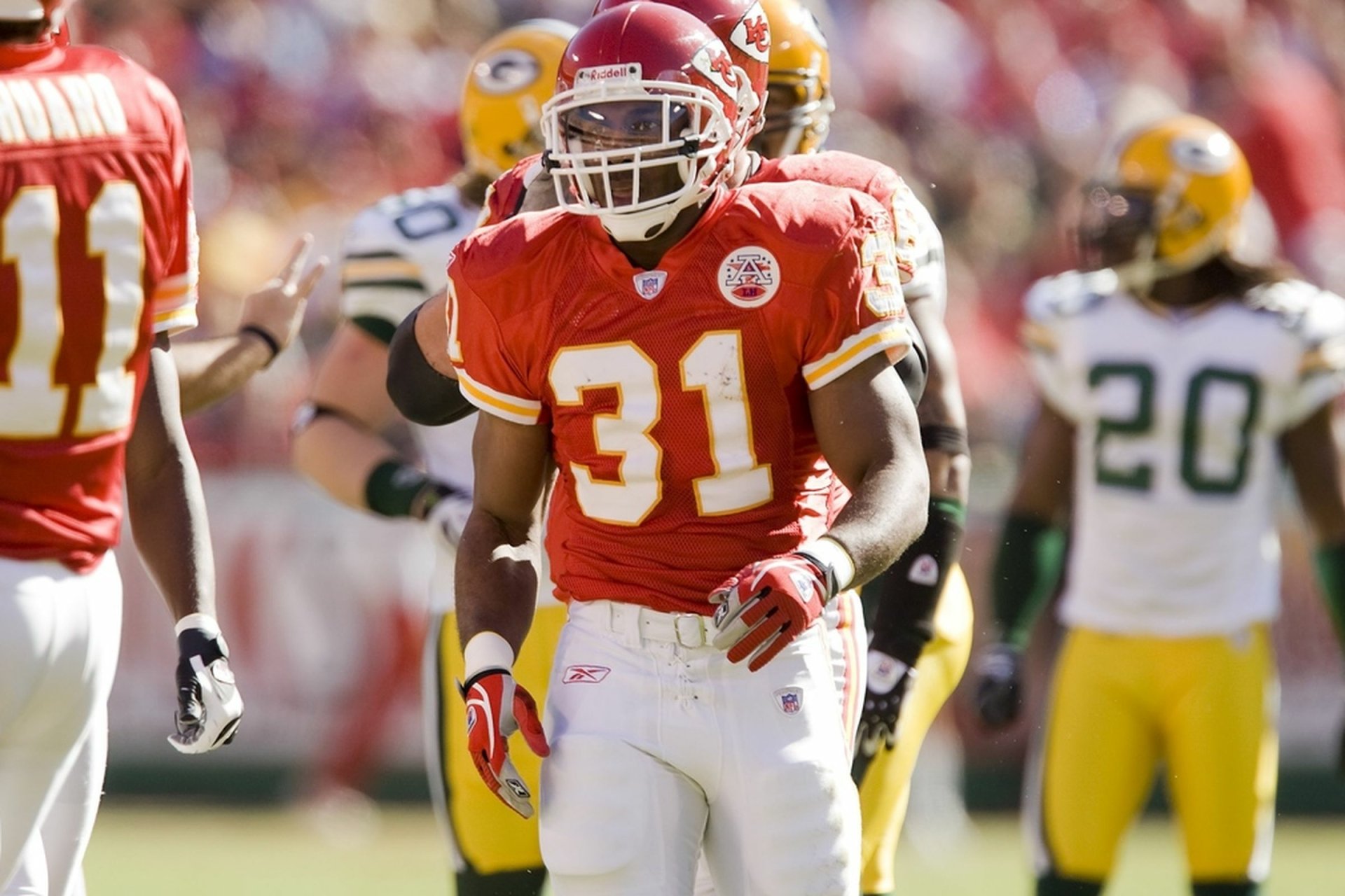 HD desktop wallpaper featuring a Kansas City Chiefs player in action during a football game, with opponents in green and yellow uniforms blurred in the background.
