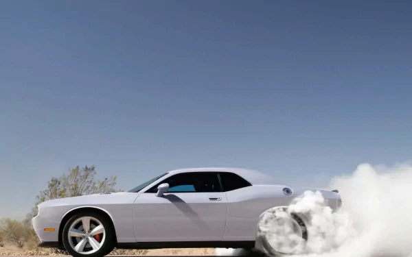 A sleek Dodge Challenger SRT8 kicks up smoke as it accelerates, showcasing its powerful design against a clear blue sky. This high-definition image serves as an impressive desktop wallpaper.