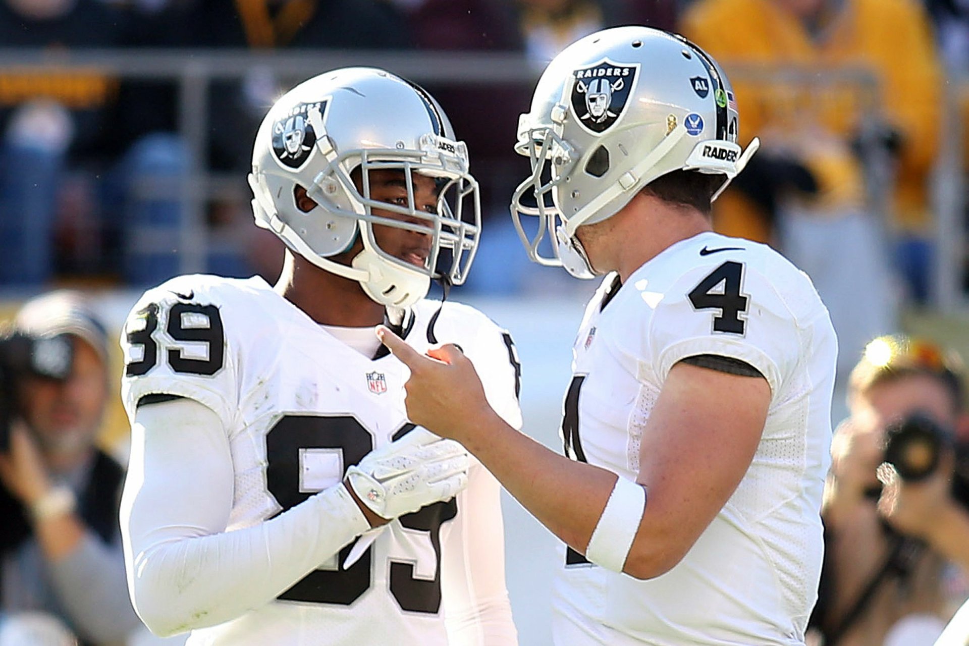 HD PC desktop wallpaper: two Las Vegas Raiders players in white uniforms conversing on the sideline during a sports game, stadium crowd background.