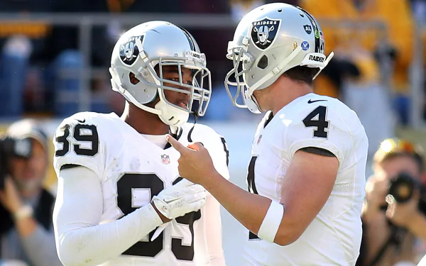 HD PC desktop wallpaper: two Las Vegas Raiders players in white uniforms conversing on the sideline during a sports game, stadium crowd background.