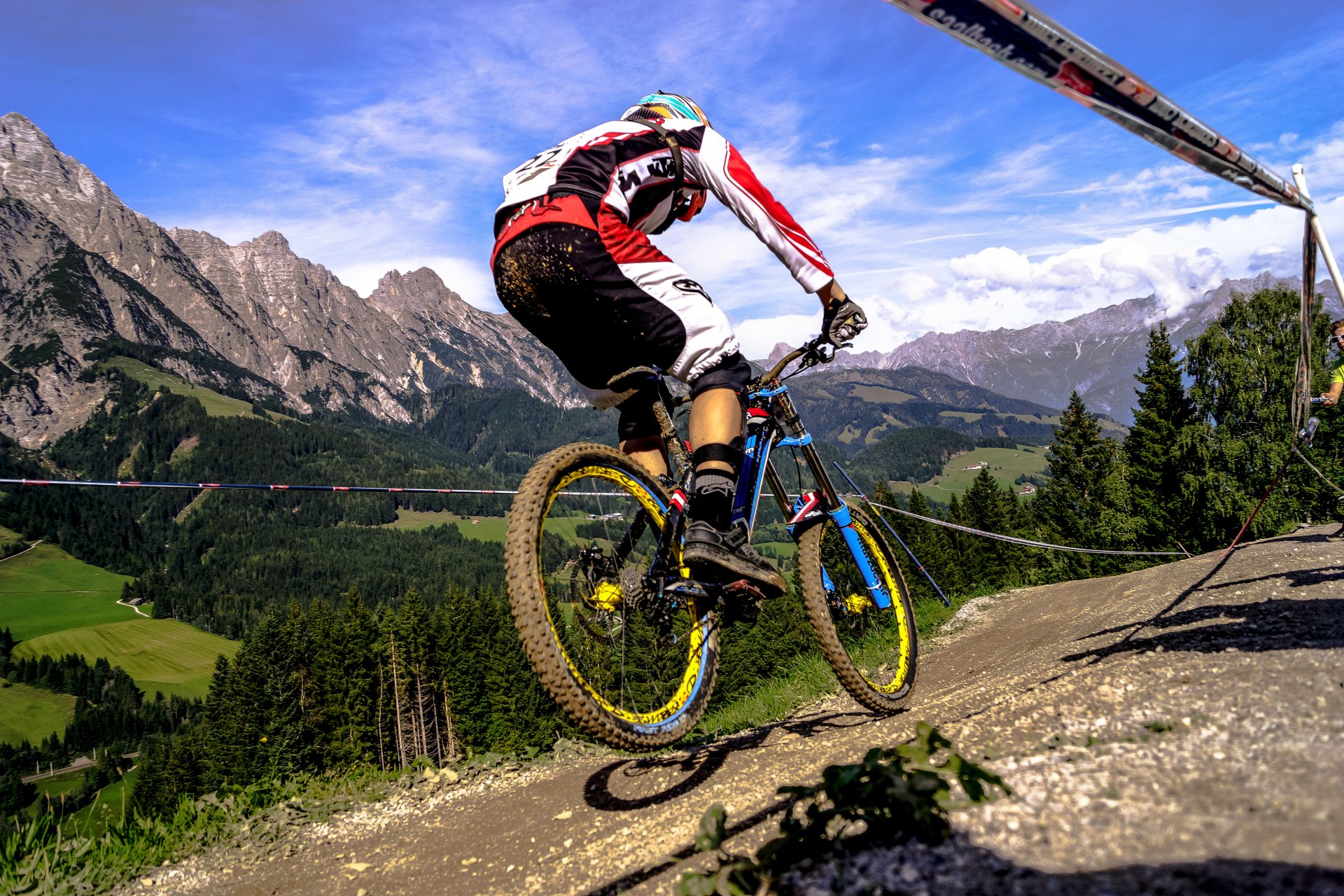 A BMX rider performs a jump against a backdrop of majestic mountains and lush greenery, capturing the thrill of sports in this stunning 4K Ultra HD desktop wallpaper.