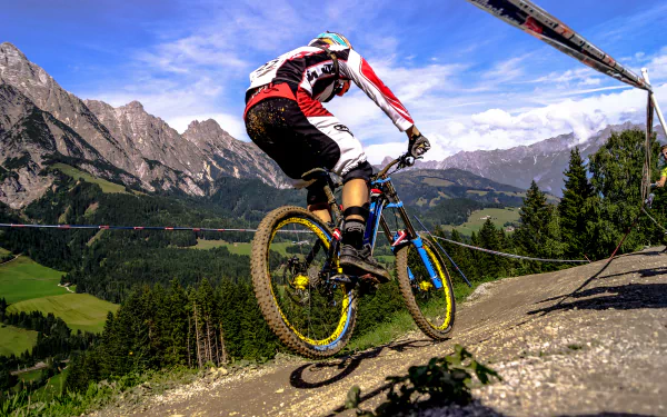 A BMX rider performs a jump against a backdrop of majestic mountains and lush greenery, capturing the thrill of sports in this stunning 4K Ultra HD desktop wallpaper.