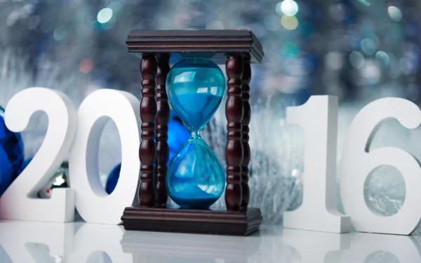 HD desktop wallpaper featuring an hourglass with blue sand between large 2016 numbers, set against a festive holiday bokeh background.