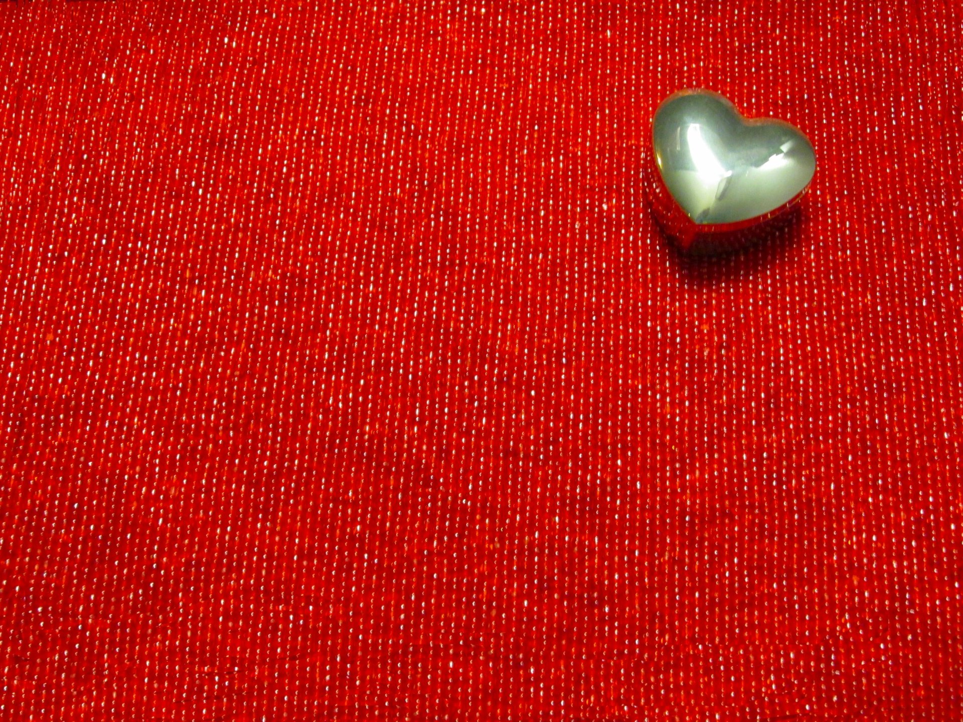 HD desktop wallpaper featuring an artistic arrangement with a shiny metallic heart on a textured red background, symbolizing love.