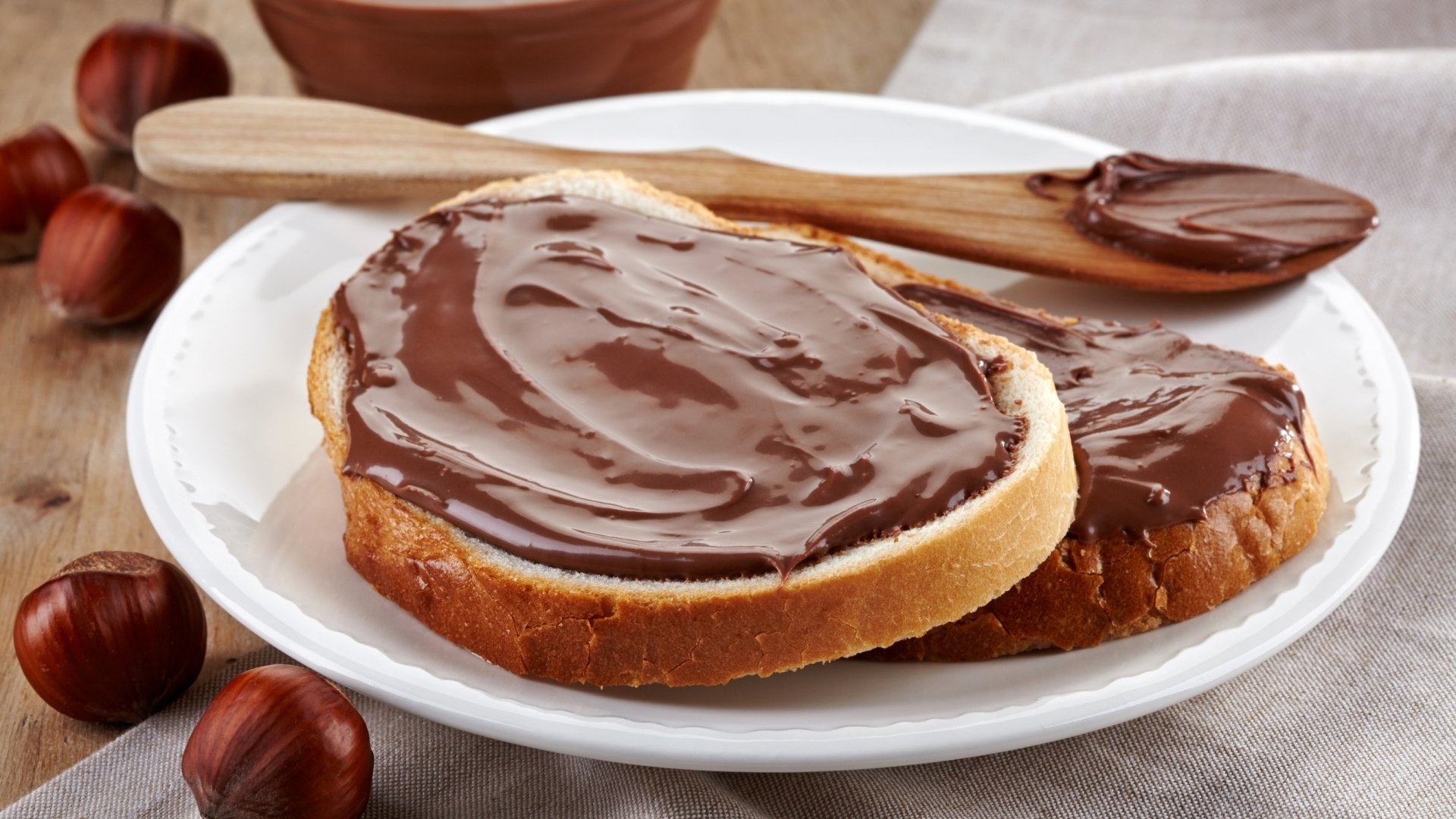 Two slices of bread spread with creamy Nutella hazelnut chocolate on a white plate, captured in high-definition for a food dessert-themed PC desktop wallpaper.