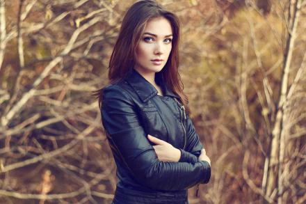 HD PC desktop wallpaper/background: woman model with long brown hair in a black leather jacket standing before tangled autumn branches, arms crossed.