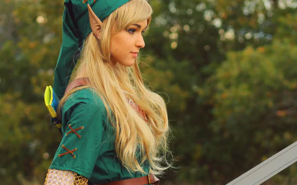 A woman in elf cosplay, featuring long blonde hair and a green outfit, stands poised with a sword, set against a lush outdoor background. A striking HD desktop wallpaper.