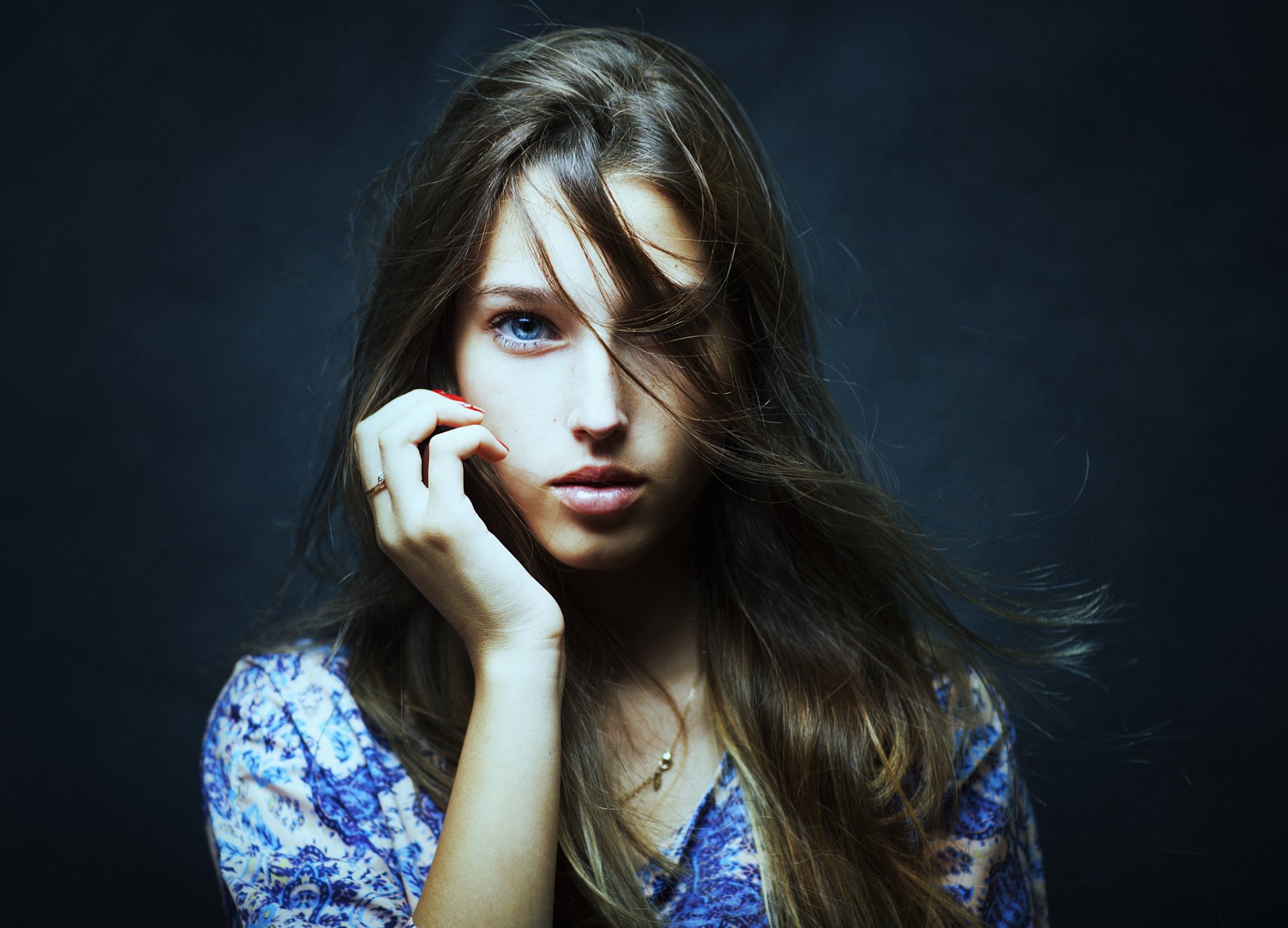 HD desktop wallpaper featuring a brunette woman with blue eyes and flowing hair, striking a captivating pose against a dark background.