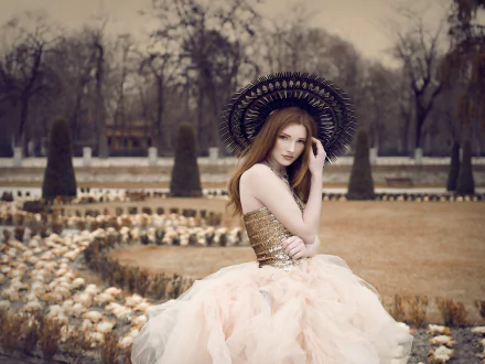 A brunette woman model in a flowing dress and decorative hat poses outdoors in a park with a bokeh background, captured in a high-definition desktop wallpaper image.