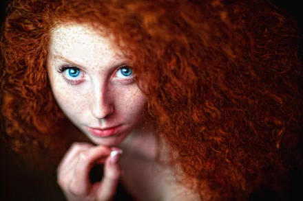 Close-up of a redhead model with blue eyes and freckles, featuring voluminous curly hair, captured in high-definition as a striking PC desktop wallpaper.