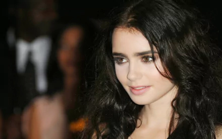 HD PC desktop wallpaper of a young woman with long dark wavy hair and soft makeup, smiling subtly against a softly blurred evening crowd background.