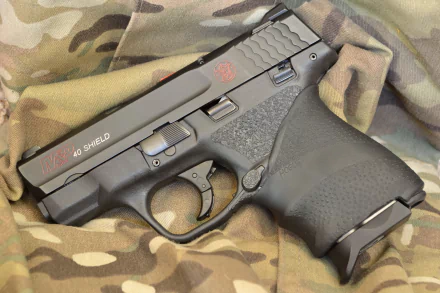 A Smith & Wesson M&P Shield pistol rests on a camouflaged fabric background, showcasing its sleek design and man-made craftsmanship in a high-definition wallpaper.