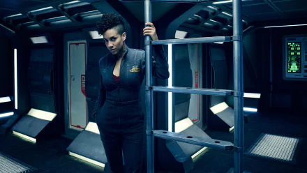 Dominique Tipper as Naomi Nagata from the TV show The Expanse stands in a dimly lit spaceship interior, featured in an HD desktop wallpaper.