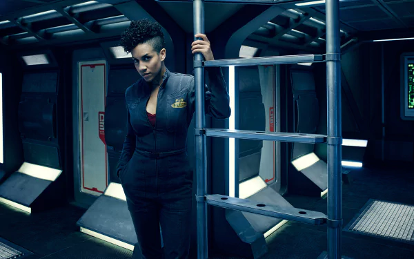 Dominique Tipper as Naomi Nagata from the TV show The Expanse stands in a dimly lit spaceship interior, featured in an HD desktop wallpaper.