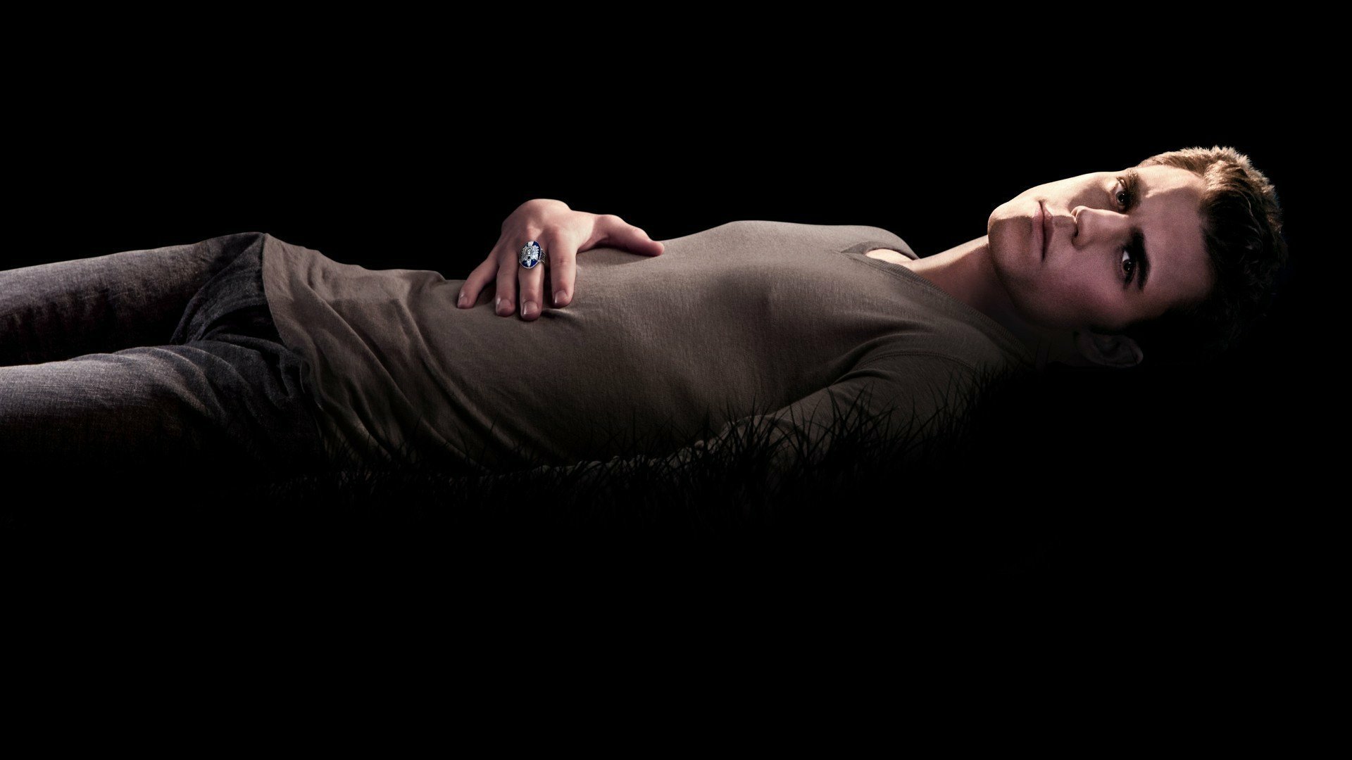 A high-definition wallpaper featuring a character from the TV show The Vampire Diaries, lying against a dark background, showcasing a moody and captivating aesthetic.