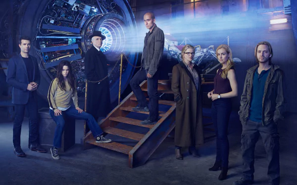 HD desktop wallpaper featuring the main cast of the TV show 12 Monkeys standing around a futuristic time machine in a dimly lit, industrial setting.