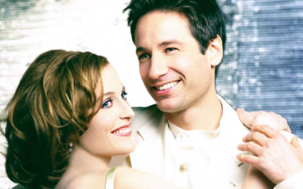 HD desktop wallpaper featuring agents Mulder and Scully from the TV show The X-Files, smiling against a blurred metallic background.