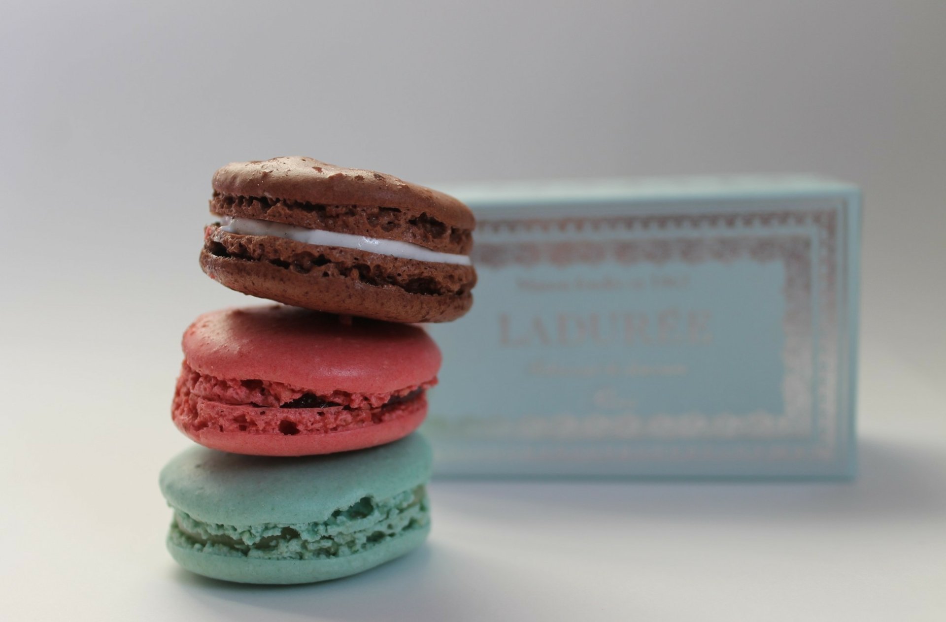 HD desktop wallpaper featuring a stack of colorful macarons with a soft-focus Ladurée box in the background, highlighting sweets and food themes.