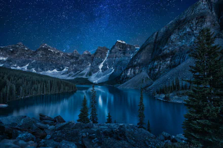A stunning winter night scene at Moraine Lake, featuring a starry sky, snow-covered mountains, and tranquil waters reflecting the beauty of nature.