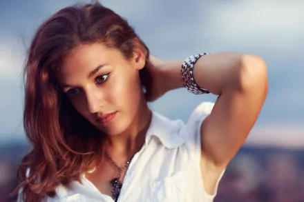 HD desktop wallpaper of a brunette woman model with brown eyes, wearing jewelry and a necklace, set against a soft bokeh background, capturing an introspective mood.