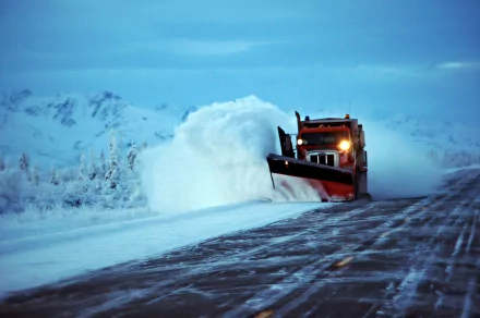 Snowplow clearing a snowy winter road against a backdrop of snow-covered mountains, captured in HD for a striking desktop wallpaper and background.