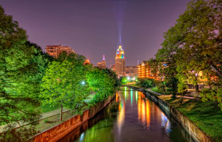 HD desktop wallpaper featuring the San Antonio city skyline in Texas, illuminated buildings, a river flanked by trees, and vibrant night lighting.