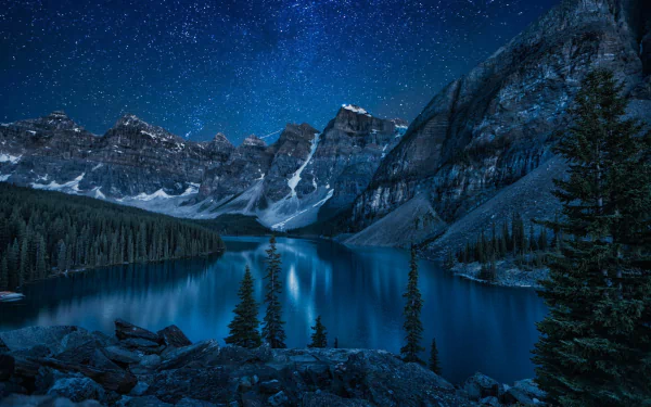 A stunning winter night scene at Moraine Lake, featuring a starry sky, snow-covered mountains, and tranquil waters reflecting the beauty of nature.
